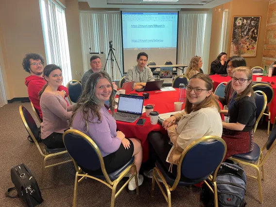 group of students are sitting around a table and smiling at the camera